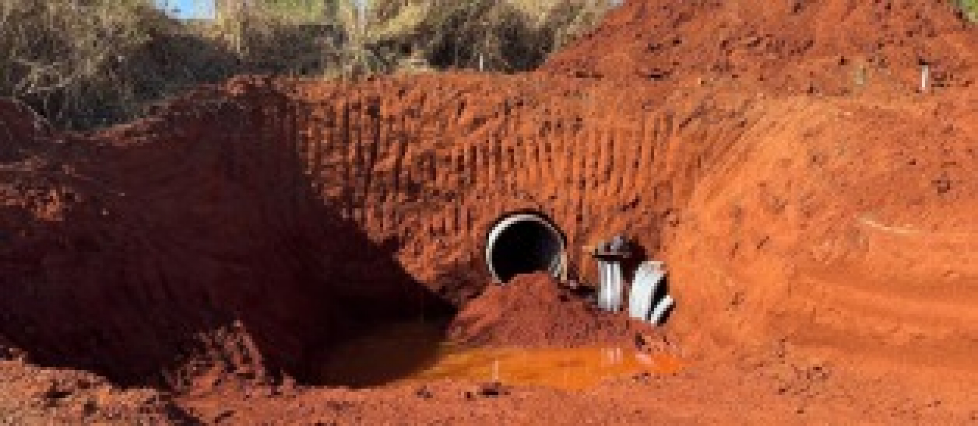 Obra de drenagem em andamento com instalação de manilhas e acúmulo de água no solo escavado.