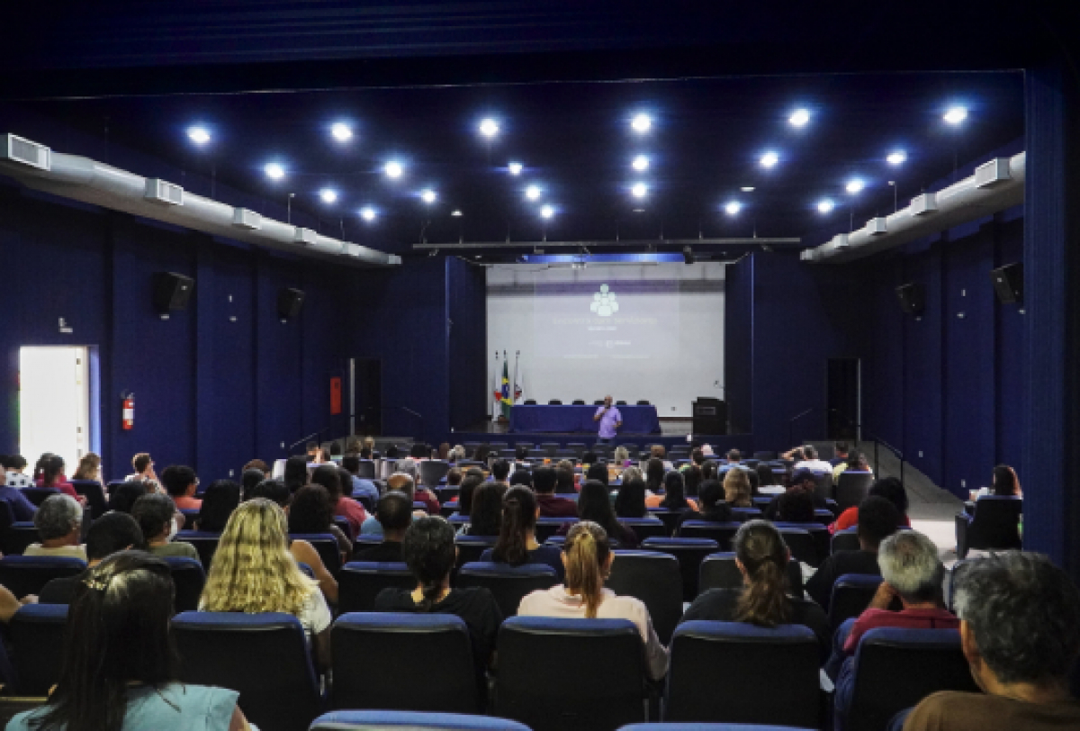 Público assistindo a uma apresentação em um auditório iluminado.