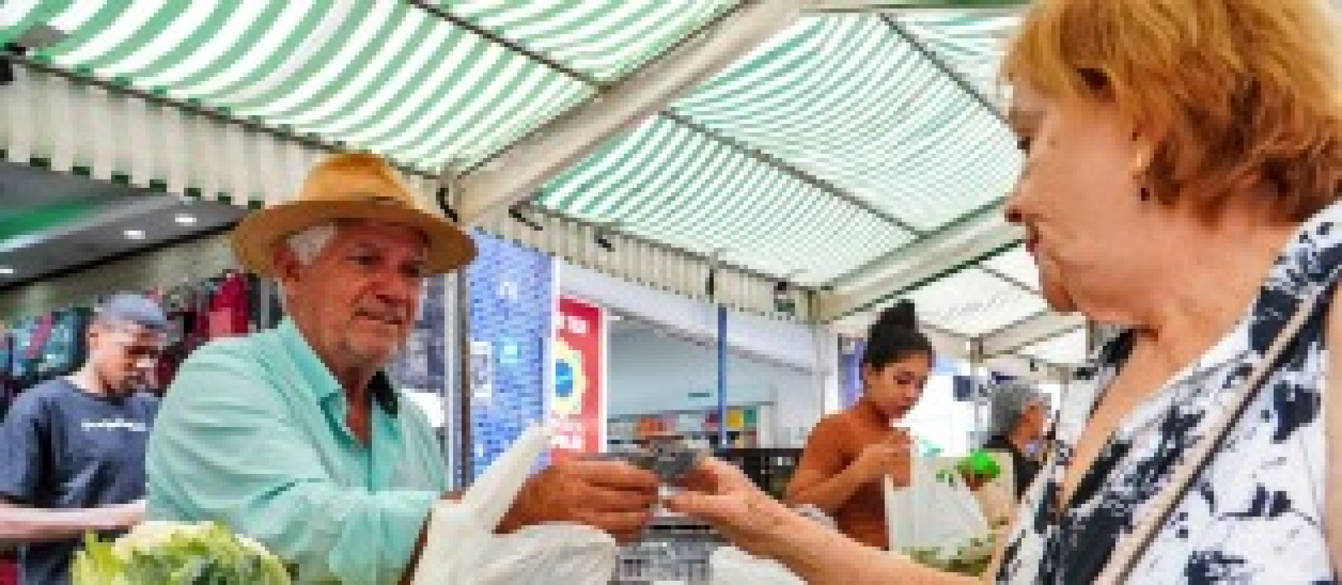 Feirante entrega produto a cliente em uma barraca de frutas e verduras.
