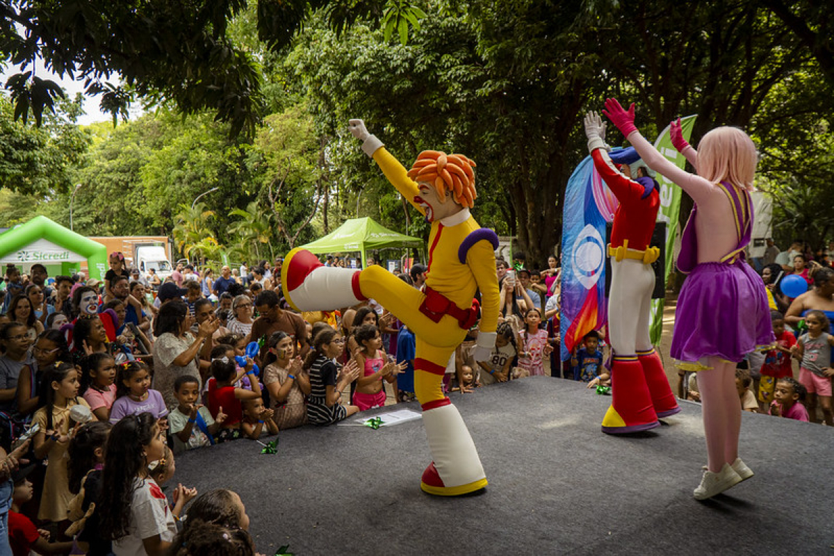 Evento infantil ao ar livre reúne crianças e famílias para assistir a apresentações de personagens fantasiados.
