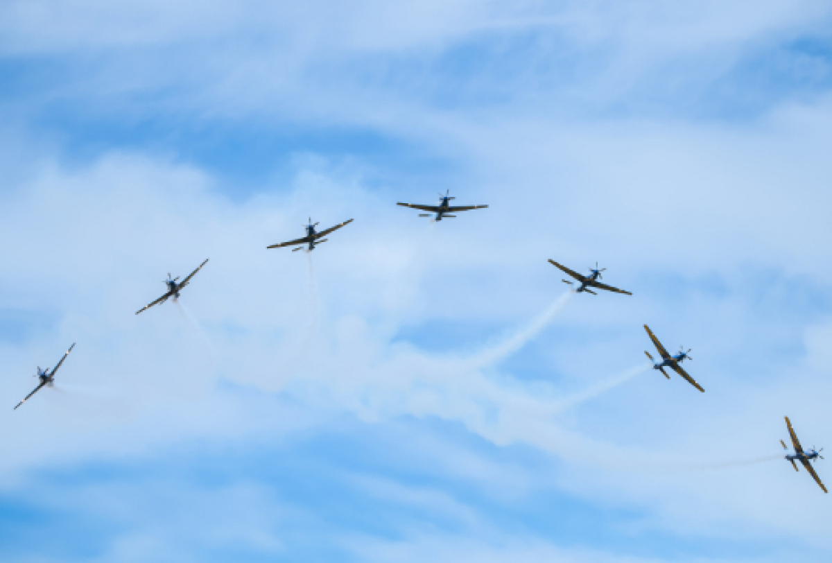 A imagem mostra aviões voando em formação, deixando rastros de fumaça no céu.