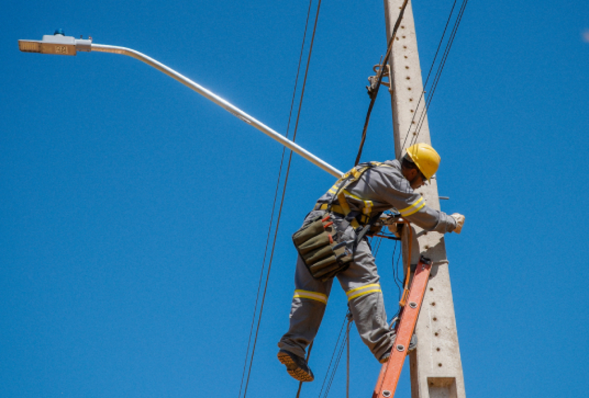 Um trabalhador em segurança realiza manutenção em sistemas elétricos em um poste de utilidade pública.