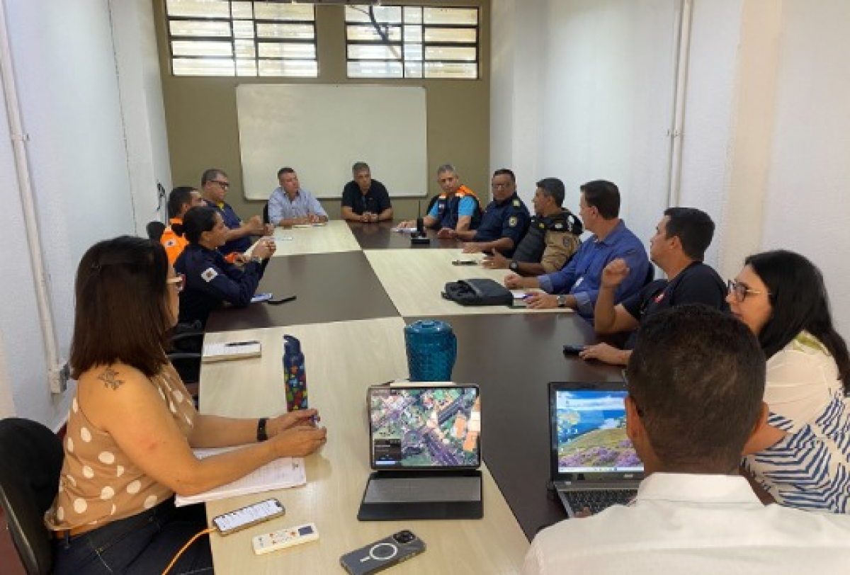 Reunião com representantes de segurança e defesa civil discutindo estratégias com apoio de mapas digitais.