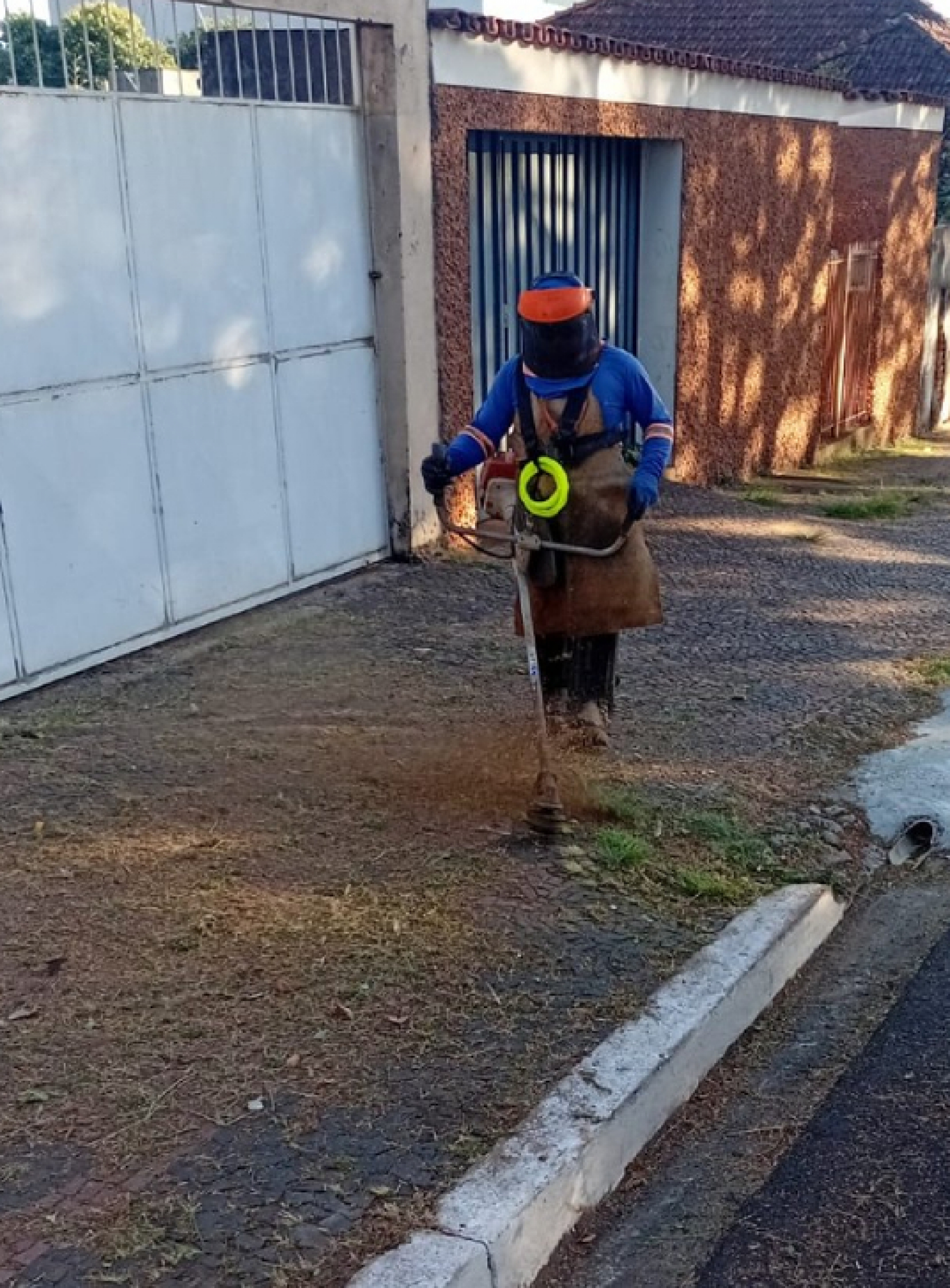 Trabalhador realiza serviço de roçagem em calçada para limpeza e manutenção urbana.          Perguntar ao ChatGPT