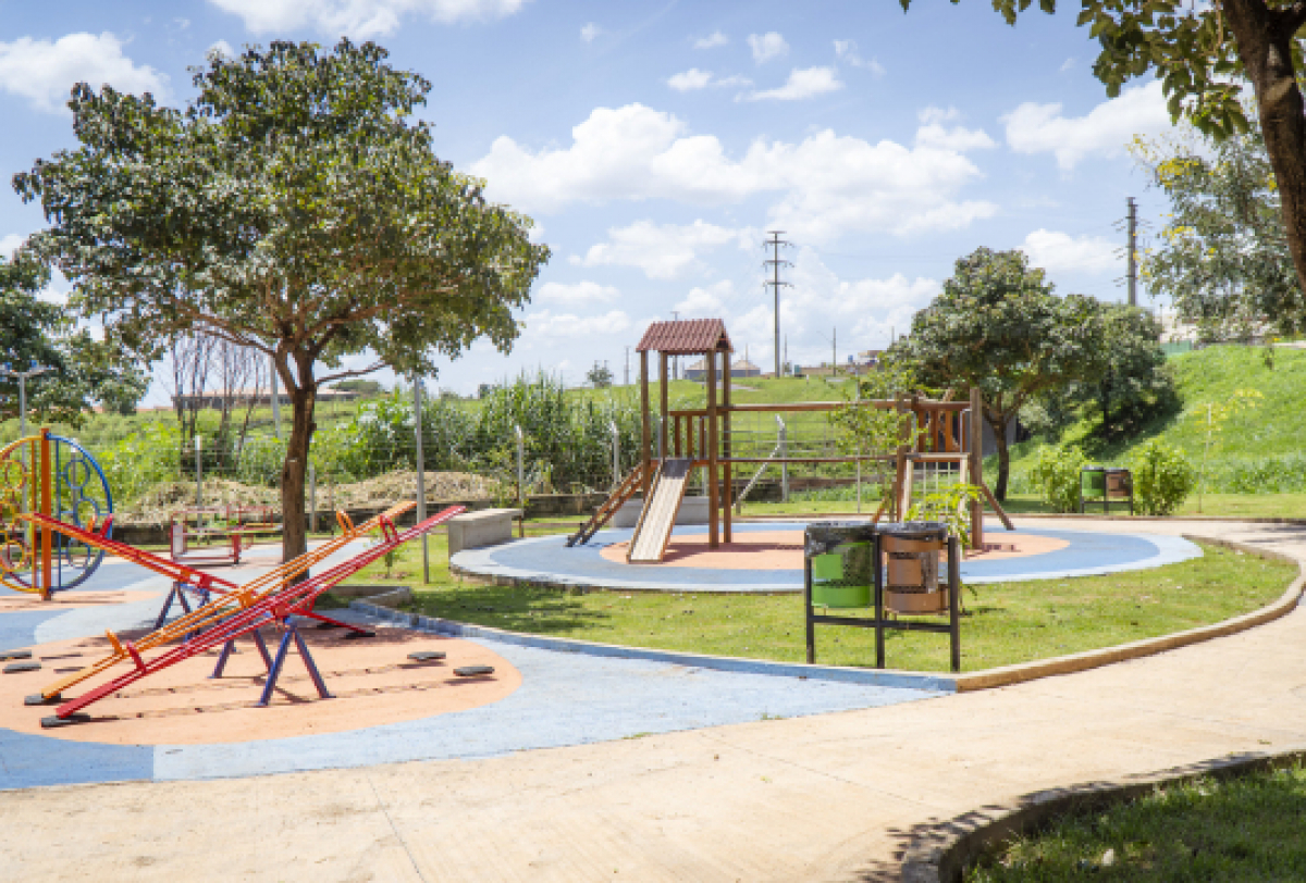 Parque infantil ao ar livre com escorregador, gangorras e árvores ao redor.