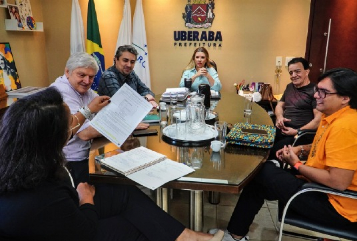 Reunião na Prefeitura de Uberaba com participantes discutindo documentos ao redor de uma mesa. 