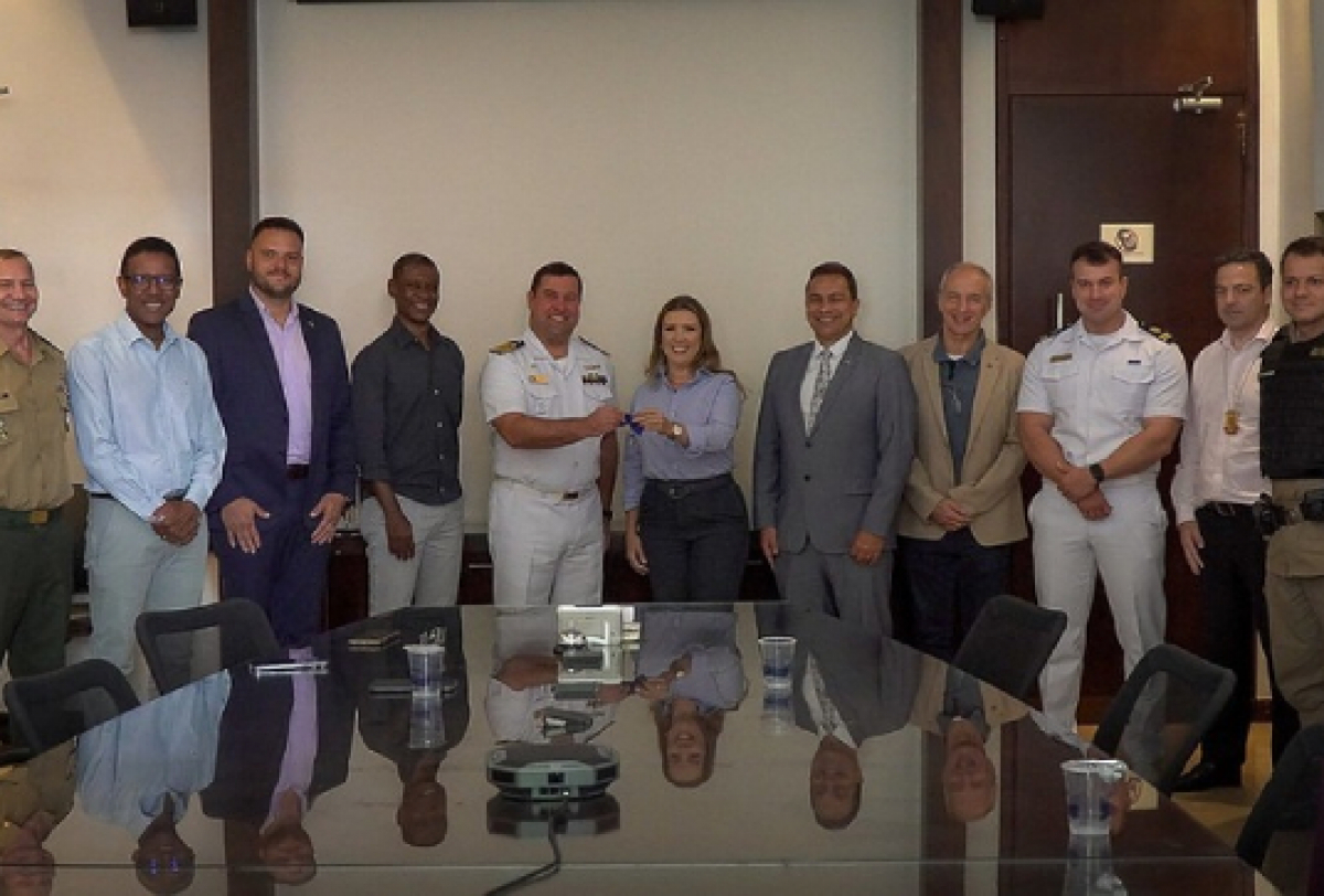 A imagem mostra um grupo de pessoas em uma sala de conferências, posando para uma foto em frente a uma mesa grande. 