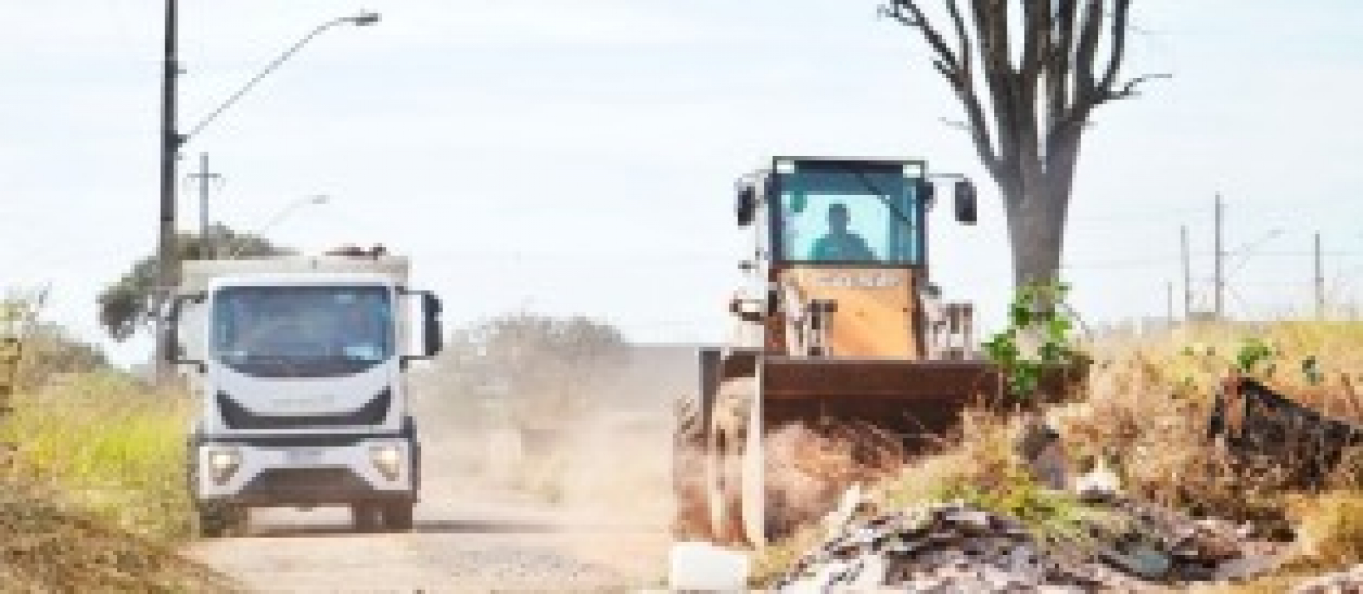 Serviços de limpeza e manutenção urbana com uso de máquina e caminhão em via pública.