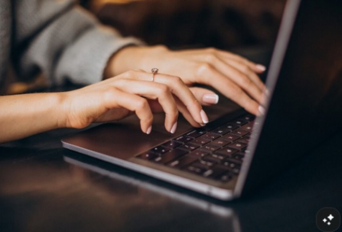 Mãos de uma pessoa digitando em um notebook, com um anel no dedo anelar.