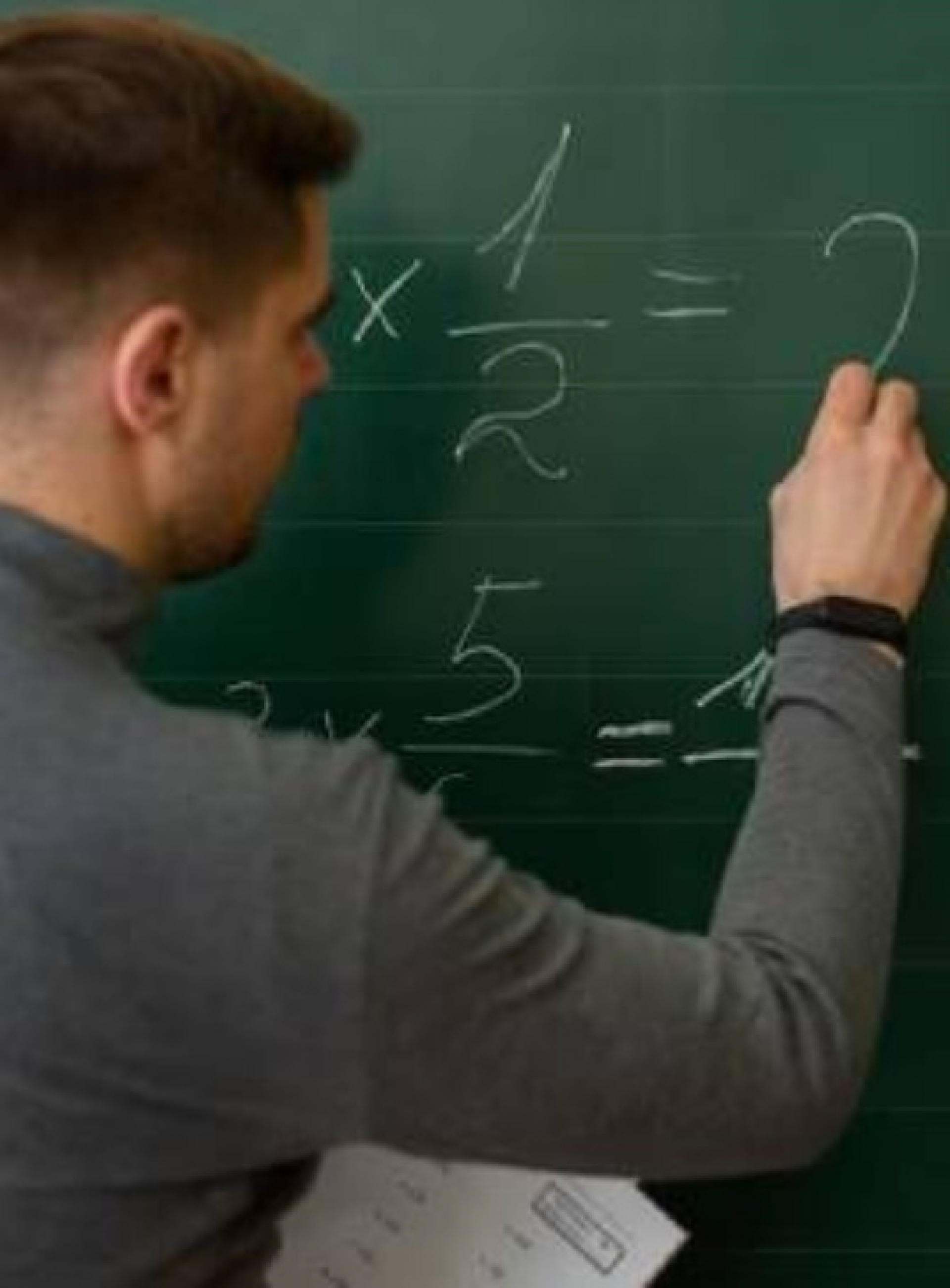 Professor escrevendo equações de multiplicação no quadro em sala de aula.