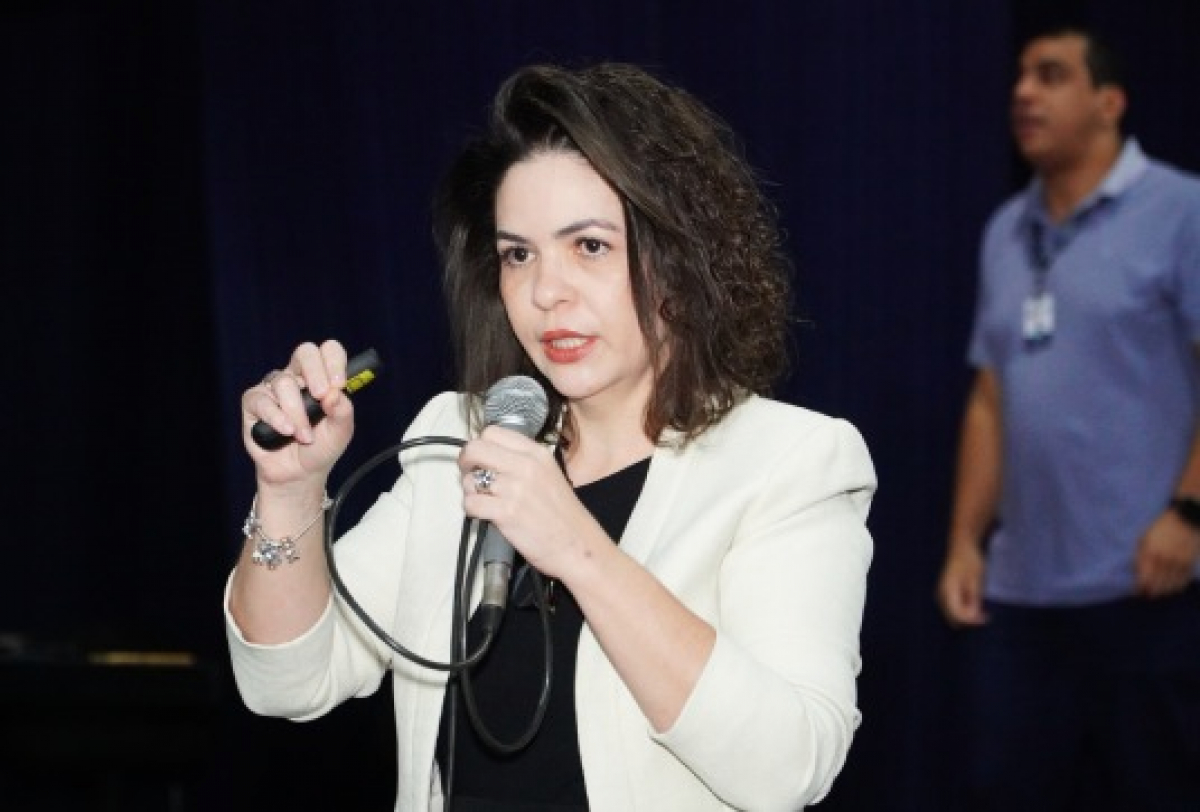 Palestrante apresenta conteúdo ao público durante evento, utilizando microfone e controle de apresentação.