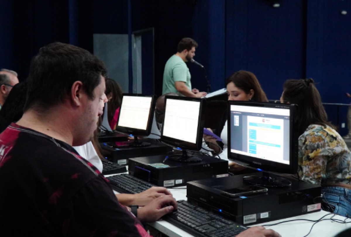 Pessoas reunidas em um escritório realizando trabalhos pelo computador.