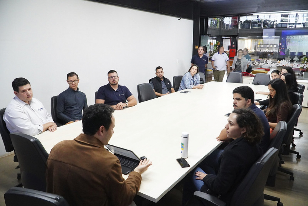 Um grupo de pessoas participa de uma reunião em torno de uma grande mesa de conferência.