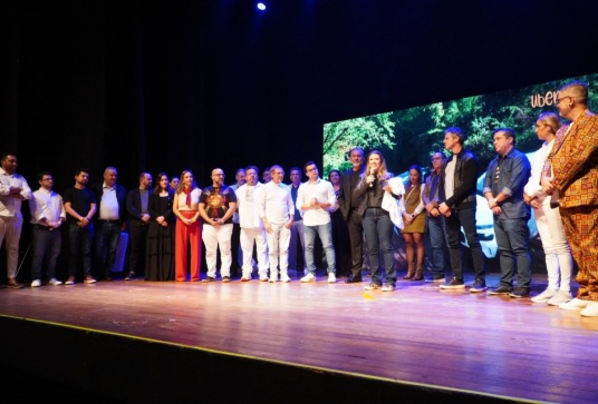 Evento corporativo com apresentação em palco, reunindo equipe diversa em ambiente formal.