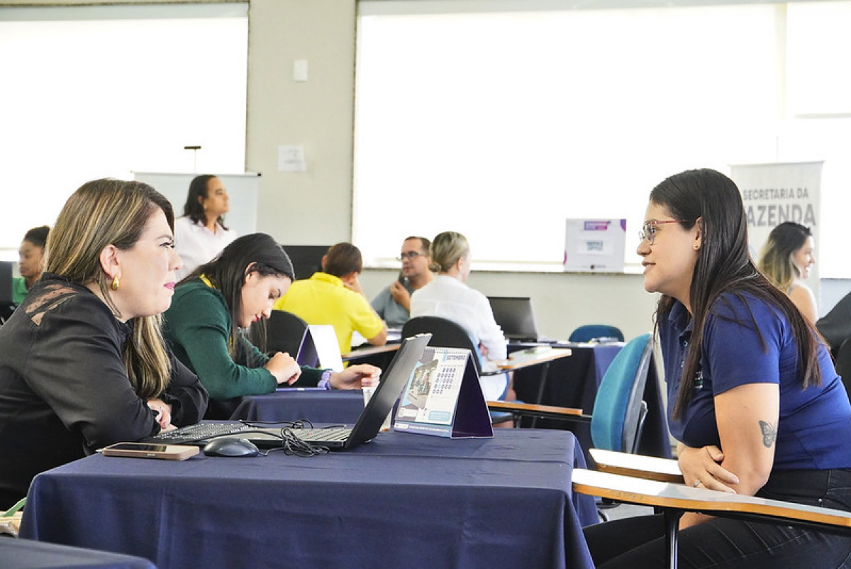 Pessoas participam de um atendimento em uma sala com notebooks.