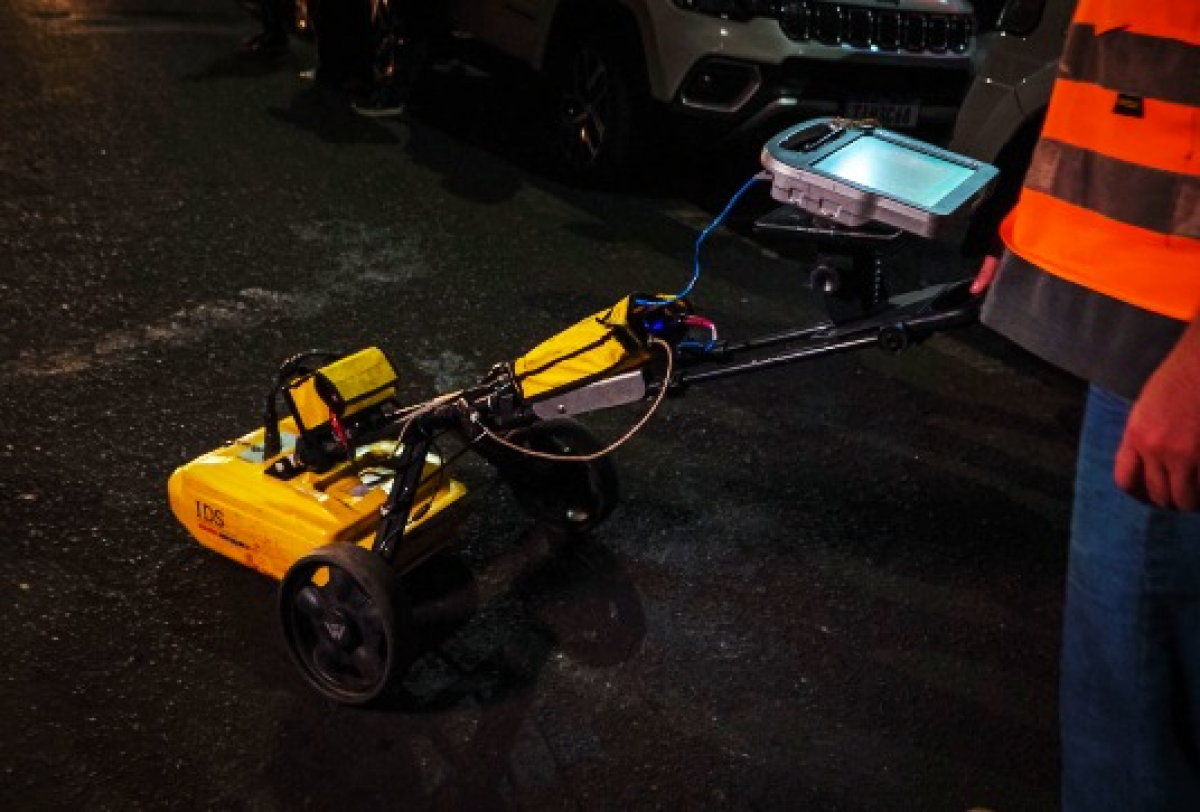 Equipamento de georradar é utilizado por técnico para inspeção subterrânea em via pública durante a noite.