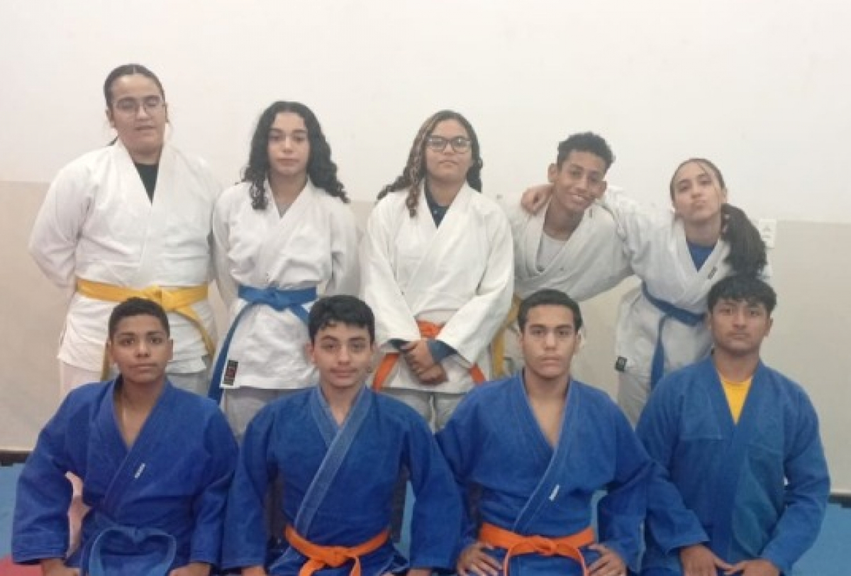 Grupo de jovens judocas posa para foto usando quimonos e faixas coloridas.