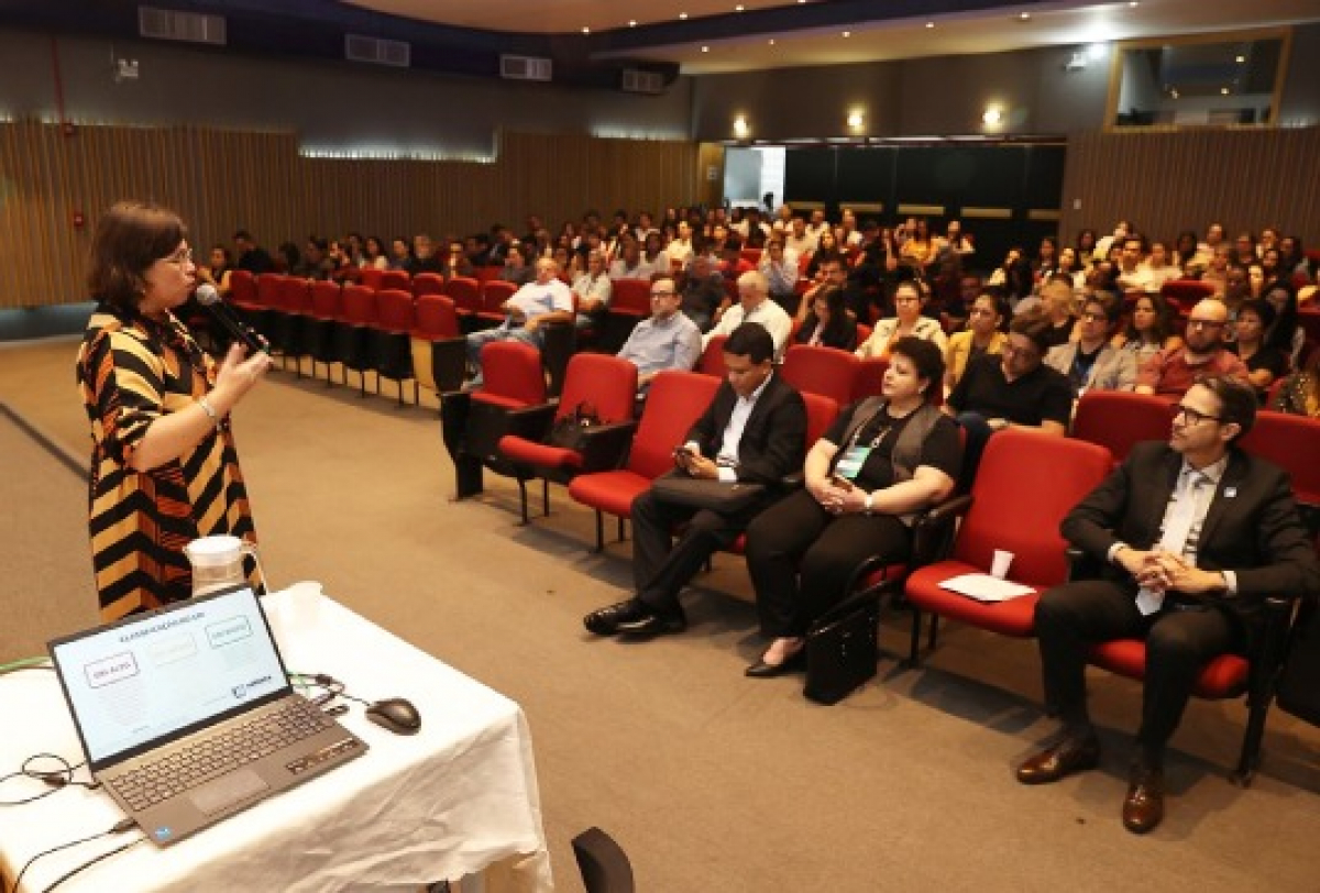 Palestrante apresenta conteúdo em auditório cheio, com plateia atenta acompanhando a exposição.