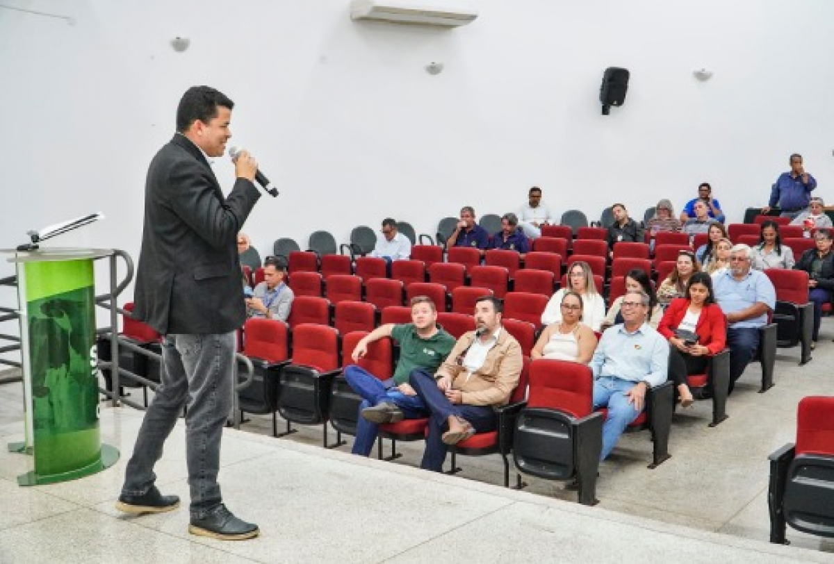 Palestrante apresenta conteúdo para um pequeno público sentado em auditório com cadeiras vermelhas.