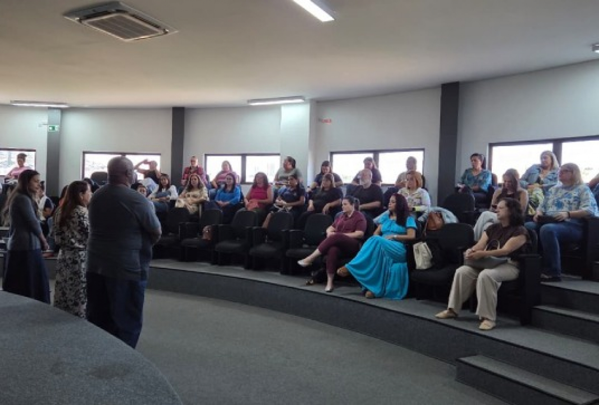 Pessoas participam de uma reunião em auditório com formato semicircular.