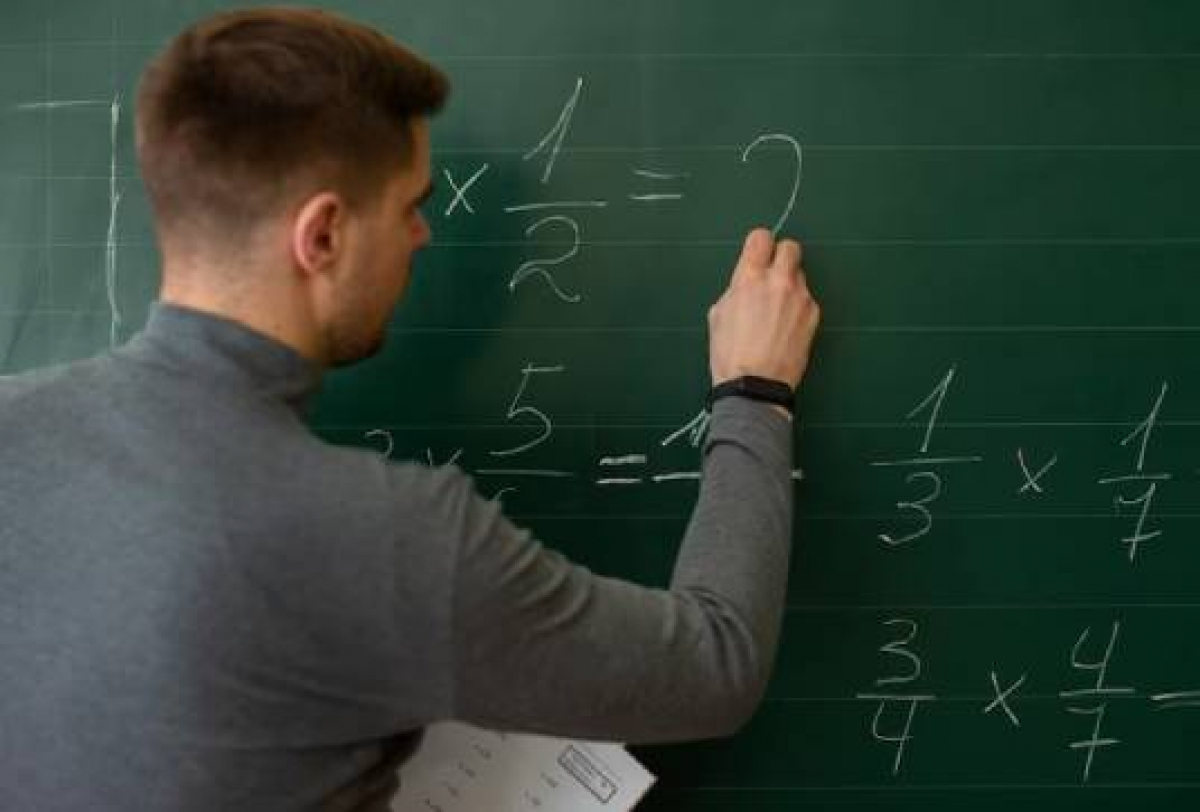 Professor escrevendo equações de multiplicação no quadro em sala de aula.