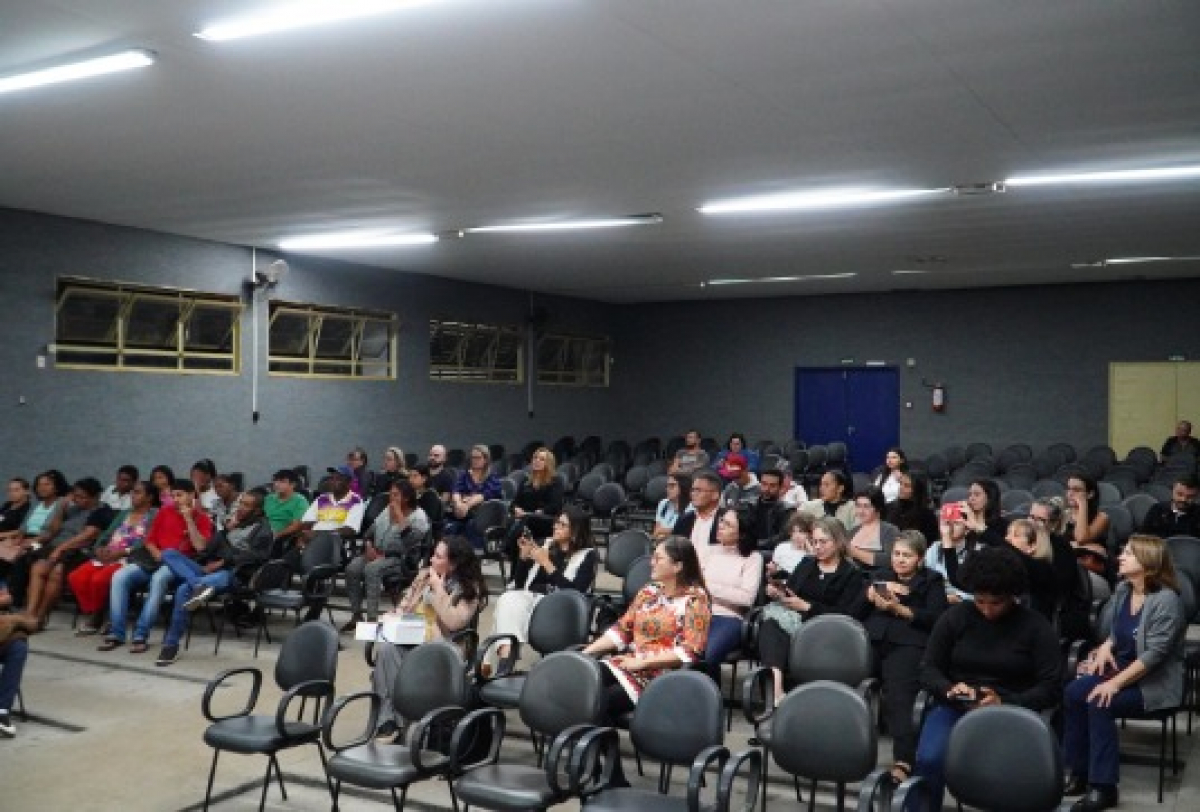 Pessoas aguardam o início de um evento em um auditório parcialmente ocupado.