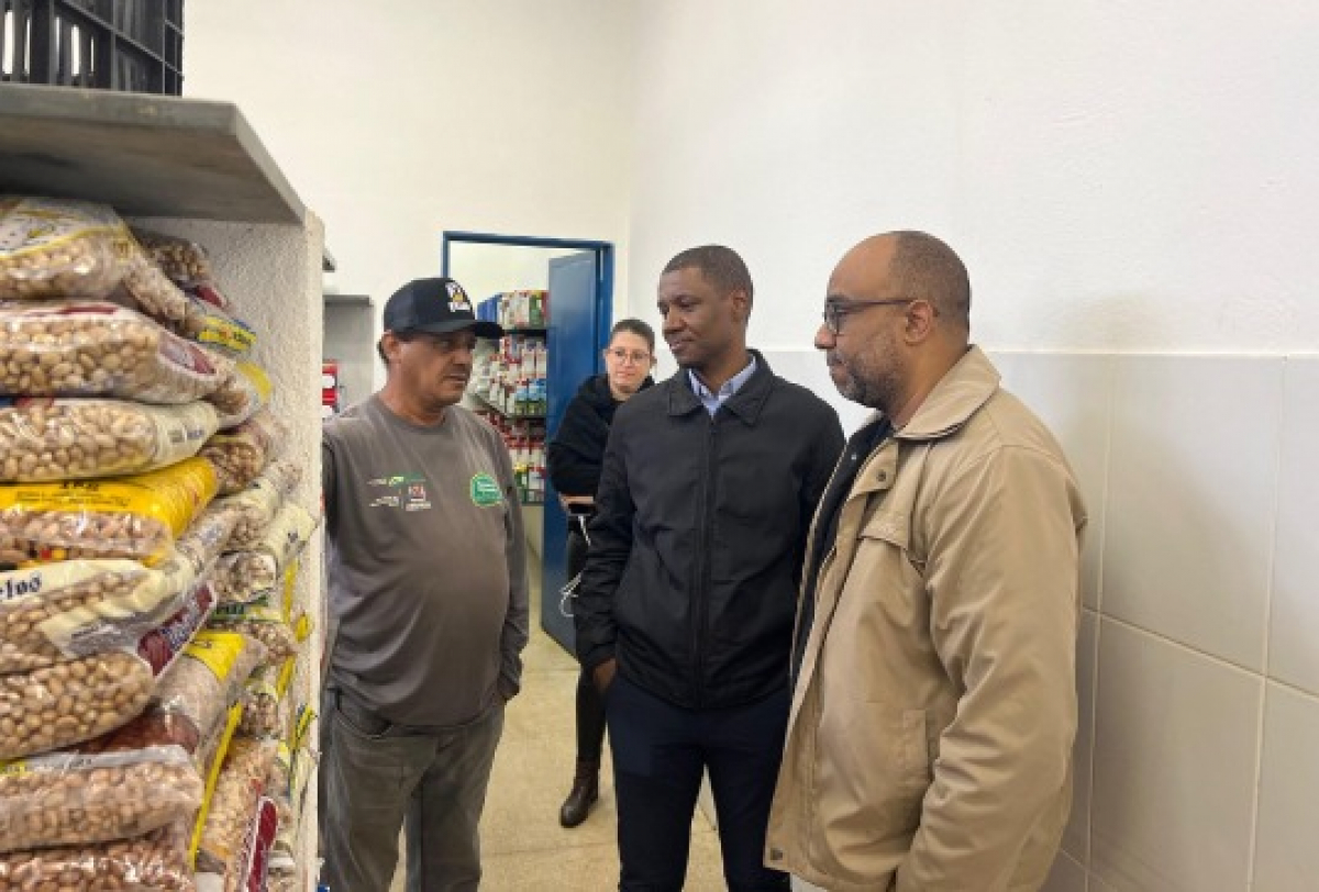 Grupo de pessoas conversa em supermercado próximo a prateleiras de alimentos.