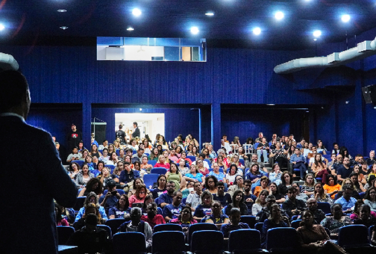 Público assiste atentamente a uma palestra ou apresentação em auditório lotado.