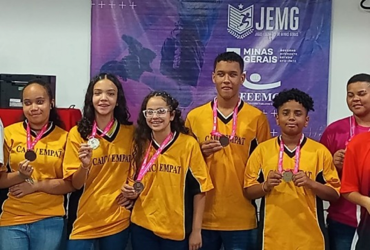 A imagem mostra um grupo de jovens estudantes com medalhas no pescoço, comemorando uma premiação dos Jogos Escolares de Minas Gerais (JEMG).