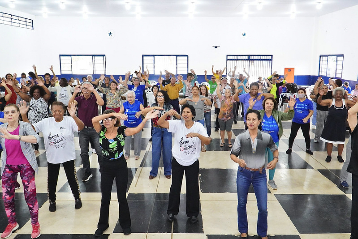 Grupo de pessoas participa de uma atividade coletiva, com muita animação, em um salão comunitário.