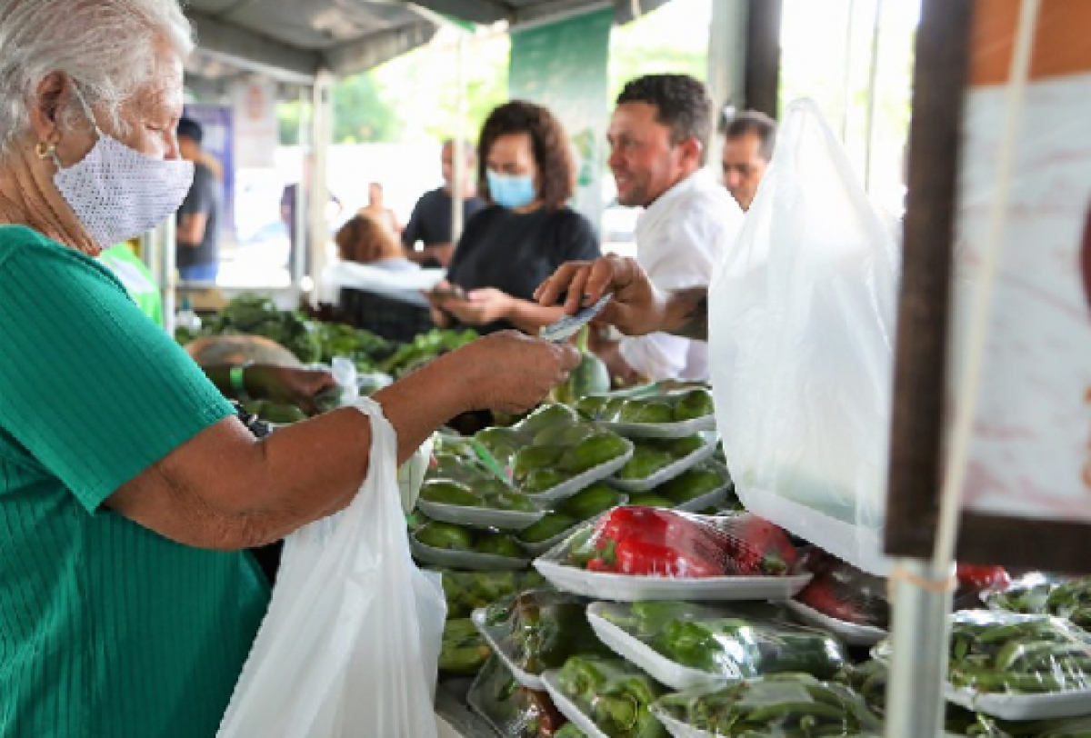 A imagem mostra uma interação em um mercado onde uma pessoa compra produtos frescos.