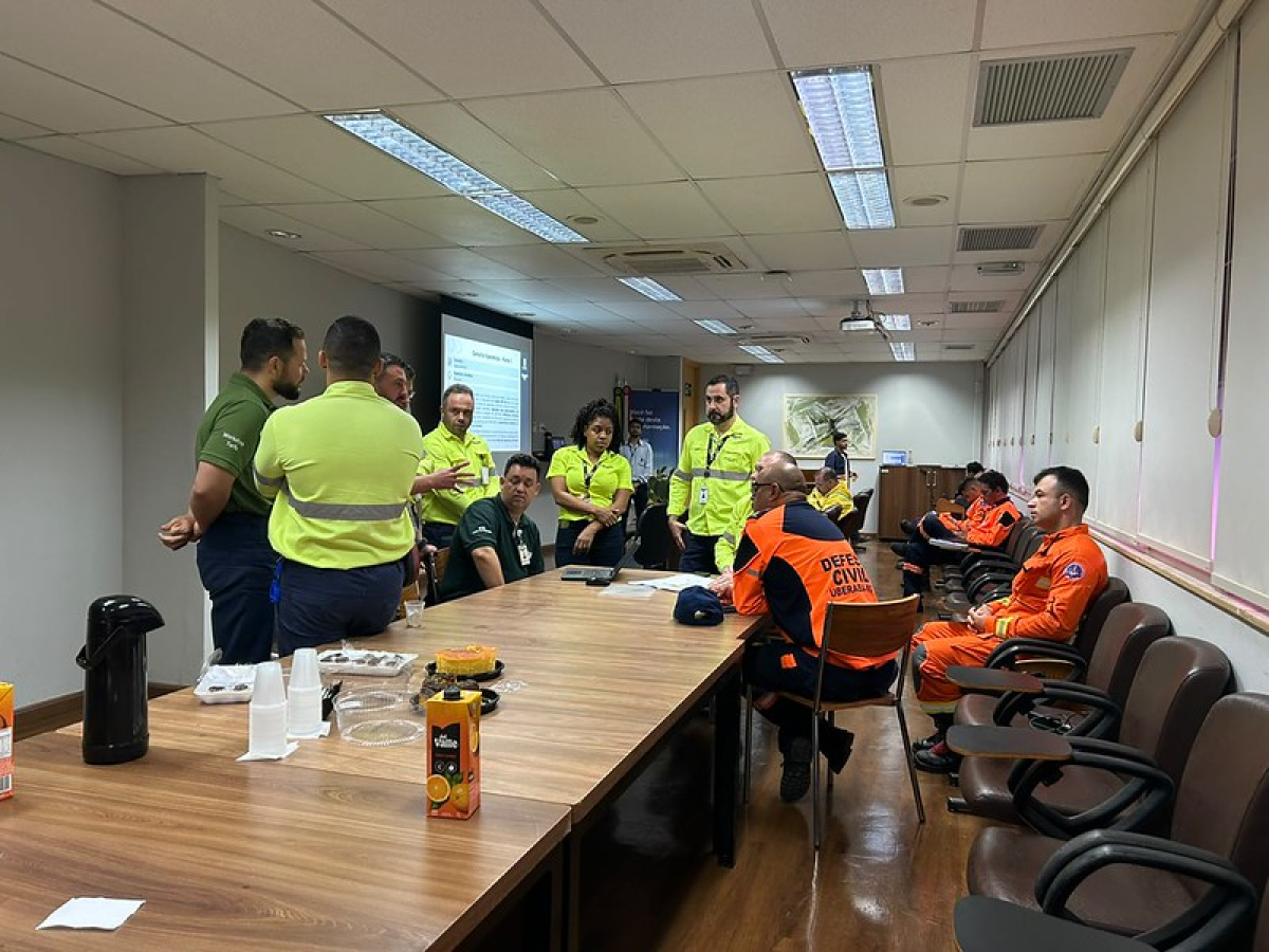 Reunião com equipes de emergência e defesa civil em uma sala, com apresentação projetada e materiais sobre a mesa.