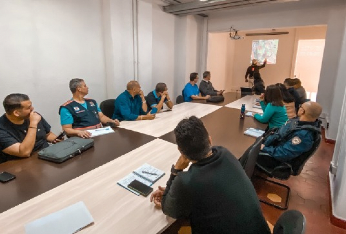 Reunião de equipe com apresentação projetada, envolvendo profissionais de diferentes áreas.