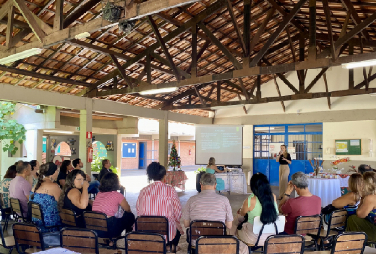 Reunião comunitária em um espaço coberto, com pessoas sentadas em círculo, assistindo a uma apresentação.