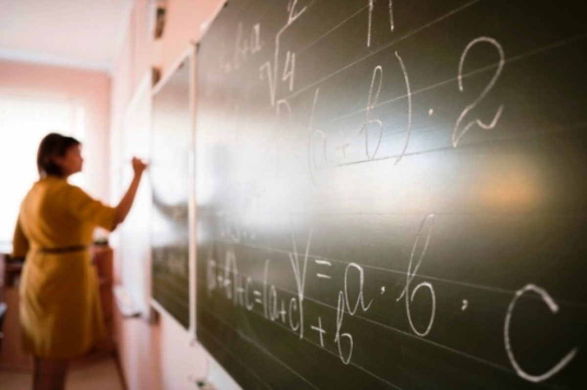 Professora escrevendo equações matemáticas no quadro em sala de aula.