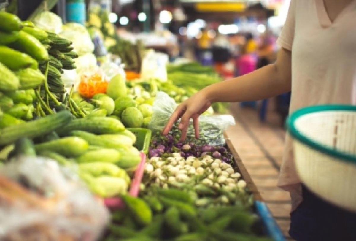 A imagem mostra uma pessoa comprando vegetais frescos em uma barraca de feira.