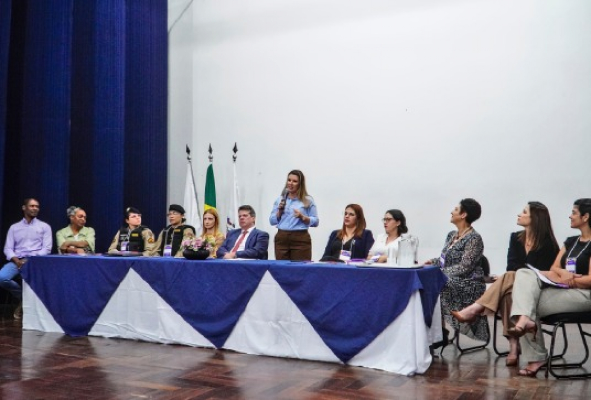 Evento oficial reúne autoridades e representantes em mesa solene com pronunciamentos ao público.