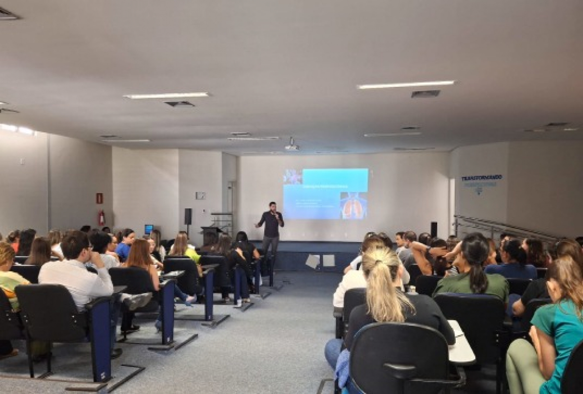 Palestra educacional em auditório com público atento e apresentação projetada ao fundo.