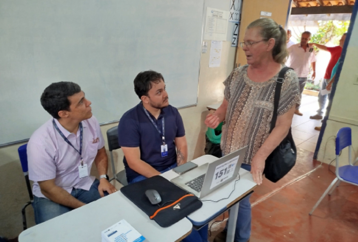 Dois servidores atendendo uma senhora em uma sala de aula.