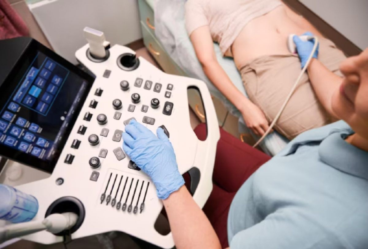 A imagem mostra uma profissional de saúde realizando um exame de ultrassonografia abdominal em uma paciente.