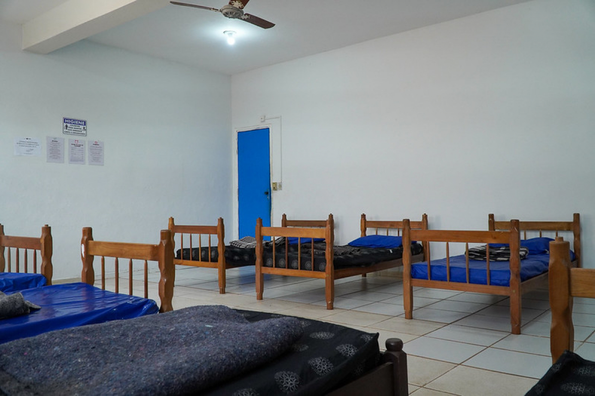 Dormitório coletivo com camas de madeira, colchões e roupas de cama, organizado em um ambiente simples e limpo.