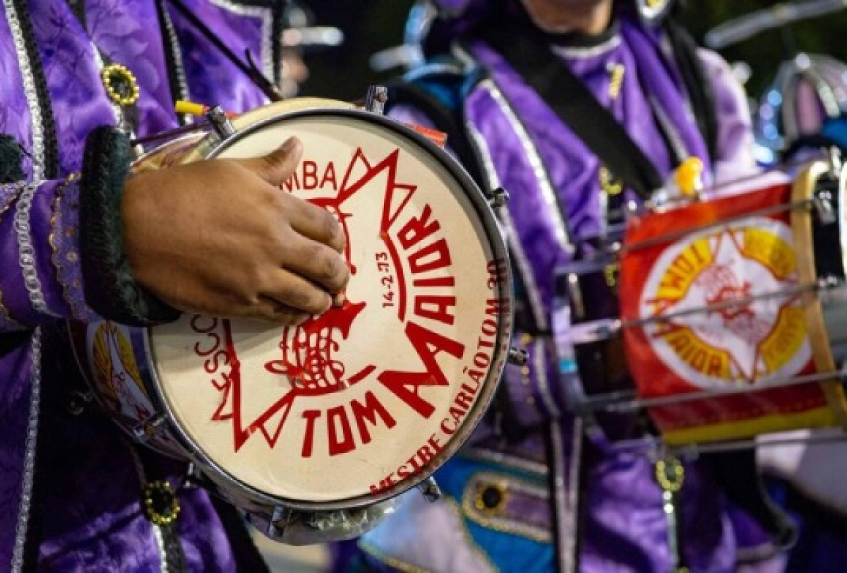 Integrantes da Escola de Samba Tom Maior tocam instrumentos de percussão em desfile carnavalesco.