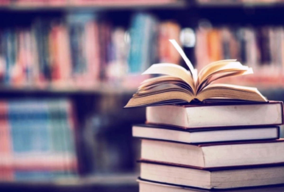 Livro aberto sobre uma pilha em uma biblioteca, destacando o ambiente de leitura e conhecimento.
