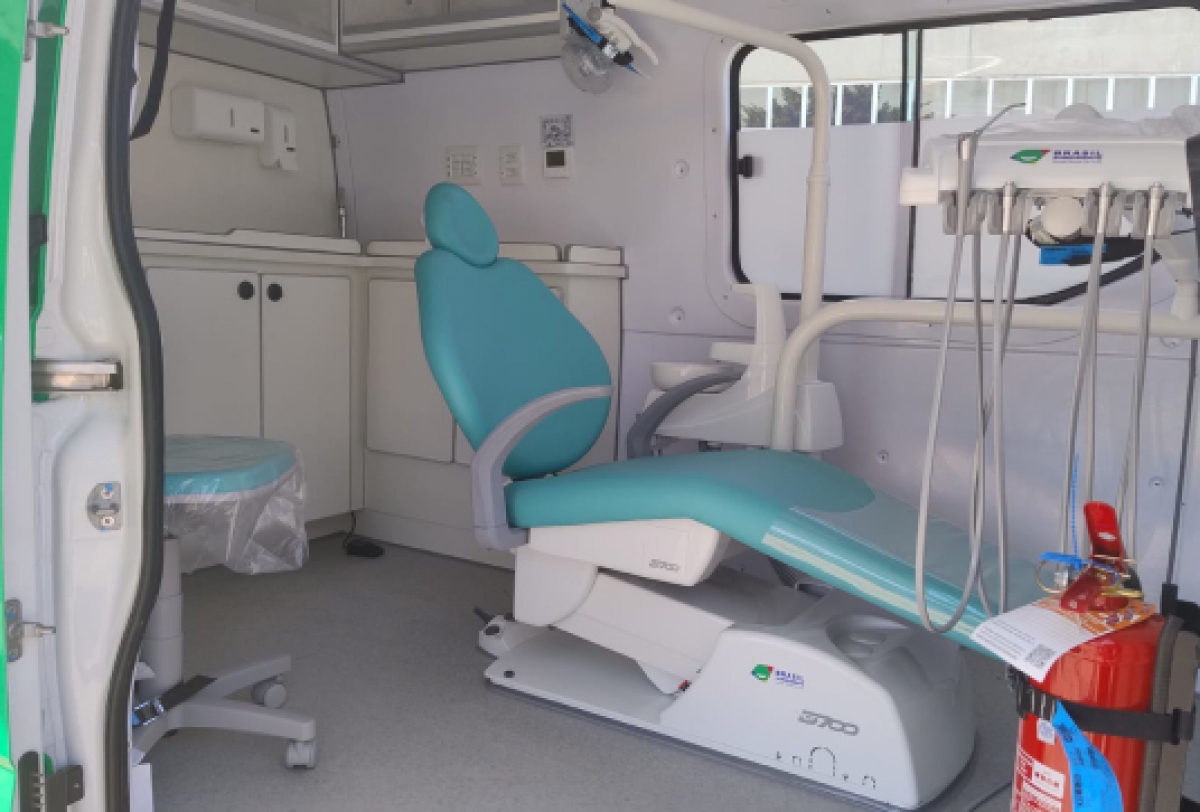 Interior de uma unidade móvel odontológica equipada com cadeira de dentista, armários e instrumentos clínicos.