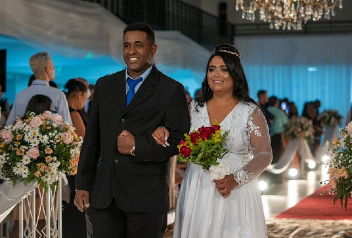 Casal sorridente caminha pelo corredor decorado em uma cerimônia de casamento.