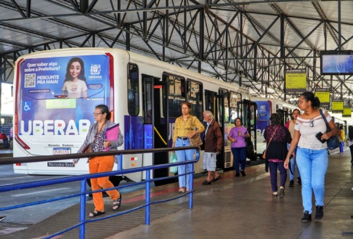 Passageiros circulando e embarcando em ônibus no terminal de transporte coletivo.