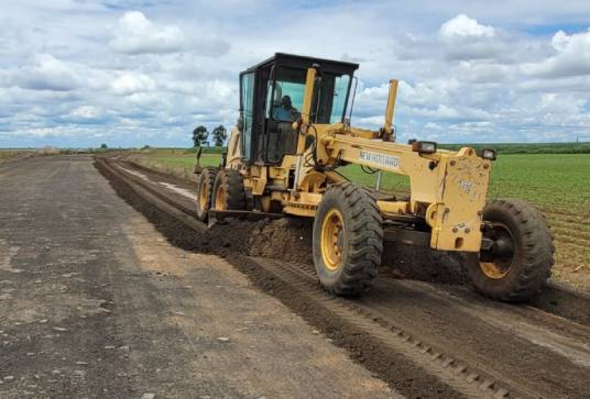 A imagem mostra uma motoniveladora amarela trabalhando na construção de uma estrada em um cenário rural.