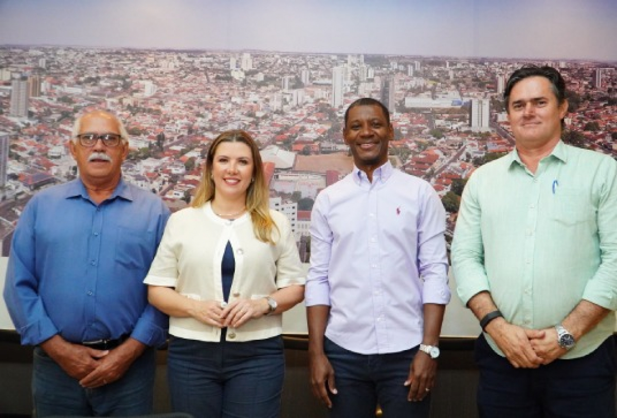 Quatro pessoas posam lado a lado para foto em frente a um grande painel aéreo de cidade.