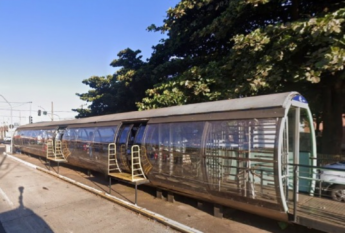 Estação-tubo de transporte público em ambiente urbano, com estrutura de vidro e metal.