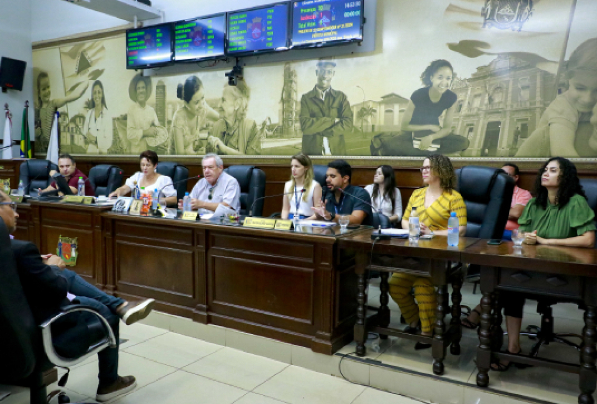 Mesa de autoridades em uma reunião formal ou sessão legislativa em um auditório.